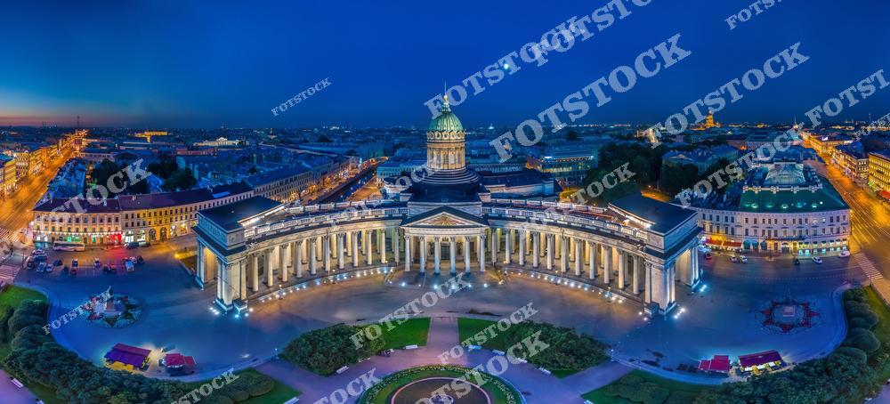 На фотографии запечатлен ночной вид на Казанский собор, расположенный на Невском проспекте в Санкт-Петербурге. Элегантные колоннады собора эффектно подсвечены, подчеркивая архитектурные детали и симметрию здания. Собор является важным историческим и культурным памятником, а его величественный фасад привлекает внимание как местных жителей, так и туристов. Окружающие улицы и здания также освещены, что создаёт атмосферу уютного и живого ночного города.